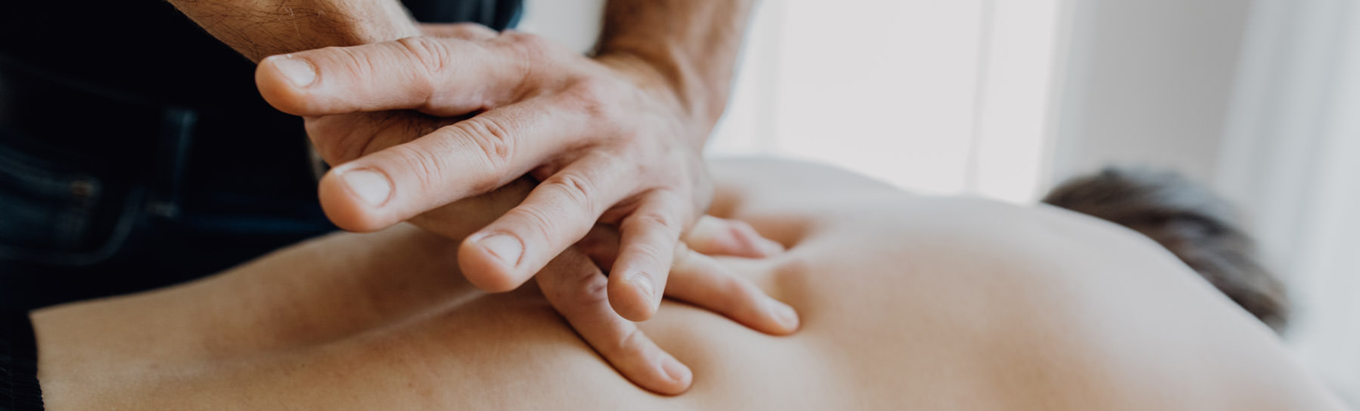 Physiotherapeut behandelt Rücken eines Patienten mit Manueller Therapie