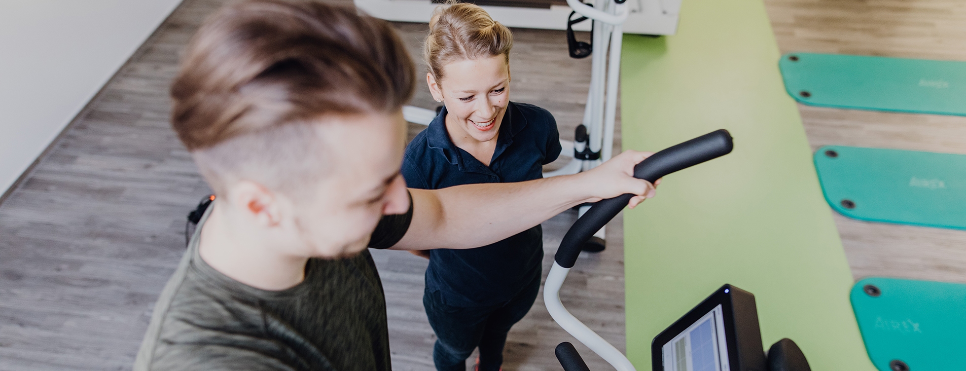 Trainerin betreut Patient auf dem Crosstrainer